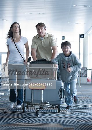Family hurrying through airport with luggage cart
