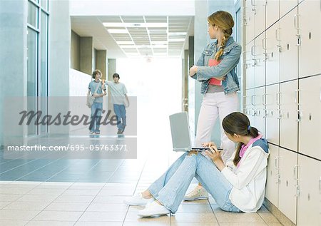 Two high school girls by lockers, watching teen boys approaching
