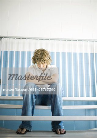 Teen boy sitting with head down on gym bleachers