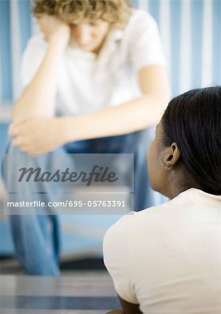 Teen boy sitting with head down, across from teen girl