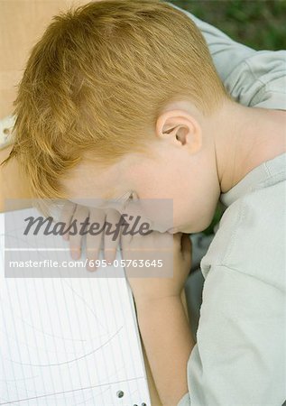 Boy with head down on table next to notebook, high angle view