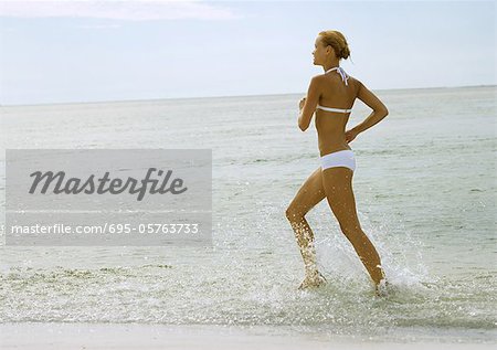 Woman in bikini running in surf at beach