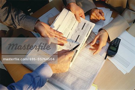 Businesspeople gesturing across table to financial pages of newspaper, cropped view