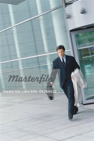 Geschäftsmann mit Aktenkoffer und Mantel über Arm, Bewegungsunschärfe zu Fuß