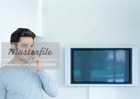 Mann mit Telefon, Breitbild-TV im Hintergrund