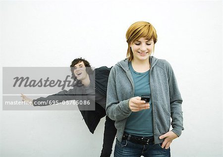 Young woman holding cell phone while young man behind her dances, white background