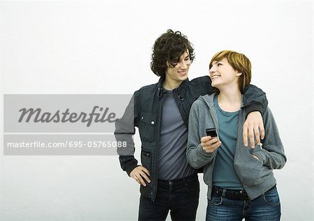 Young adult couple looking at each other, man with arm around woman, woman holding cell phone