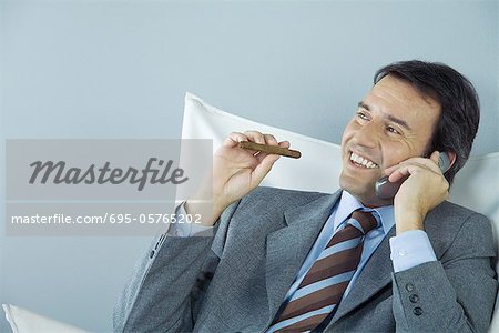 Businessman using cell phone and smoking cigar