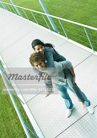 Teenage couple, boy holding girl piggyback, standing on walkway smiling at camera