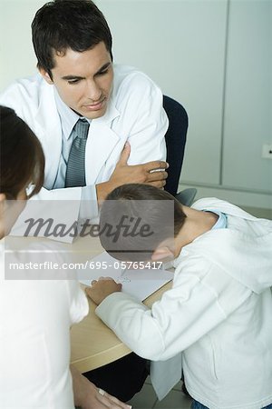 Doctor sitting with boy and woman, boy drawing on paper, high angle view