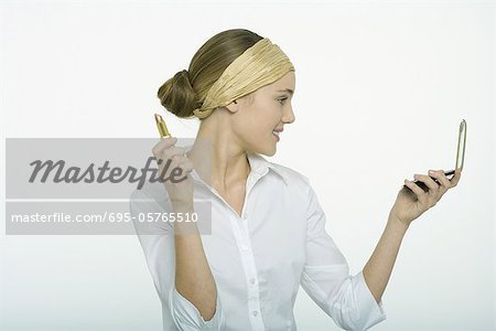 Teenage girl holding lipstick, looking at self in hand mirror