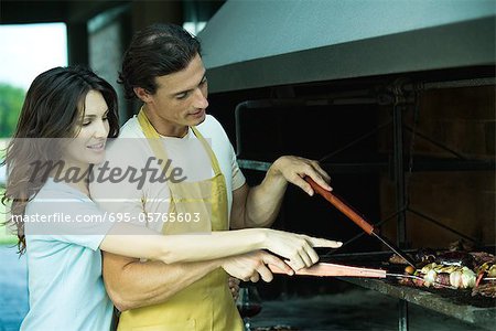 Homme qui tend à barbecue, tandis que la femme regarde par-dessus son épaule et points