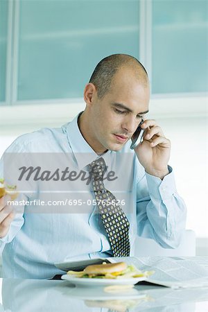 Homme assis à table, manger des hamburgers, lire le journal et l'utilisation de téléphone cellulaire