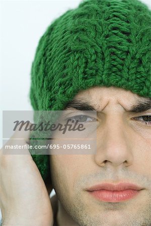 Jeune homme portant knit hat, sillonnant les sourcils, portrait, gros plan