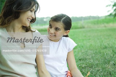 Fille et mère assis dehors, souriant à l'autre