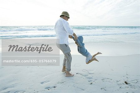 Grandfather swinging boy on beach