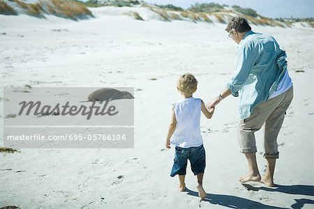 Child and adult walking on sand