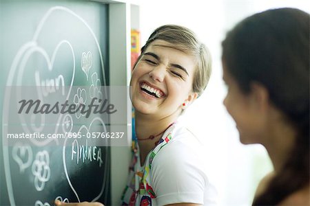 Young female friends writing names in hearts on chalkboard, laughing