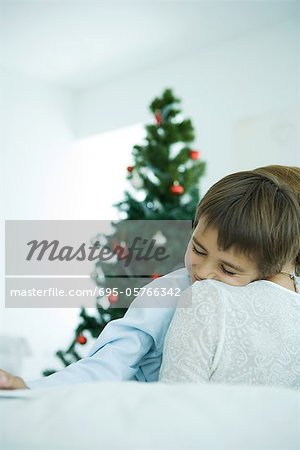 Mère assise sur le canapé, holding garçon dans les bras, arbre de Noël dans l'arrière-plan, garçon souriant