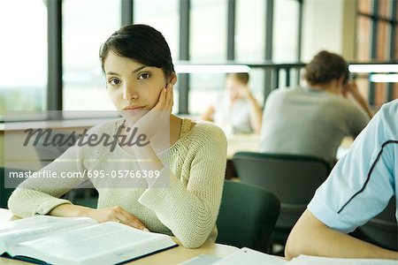 Young woman studying in university library, looking at camera