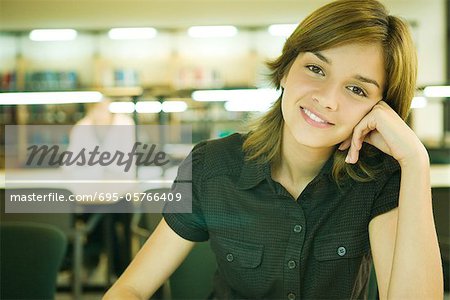 Young woman in university library, smiling at camera