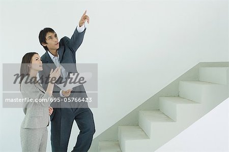 Well-dressed couple visiting house, man holding blueprint and pointing