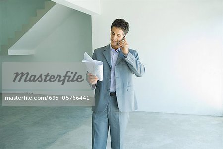 Well-dressed man looking at blueprints, using phone