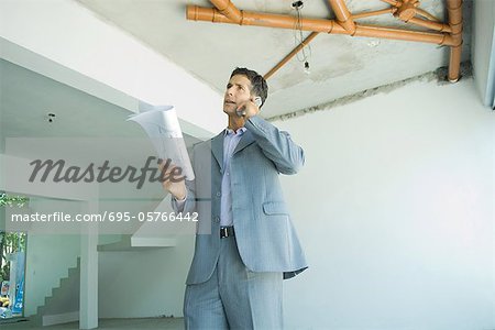 Gut gekleideter Mann, Blaupausen, mit Telefon, unvollendete home innere Inspektion