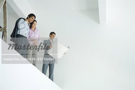 Young couple standing with architect, looking over unfinished interior, low angle view