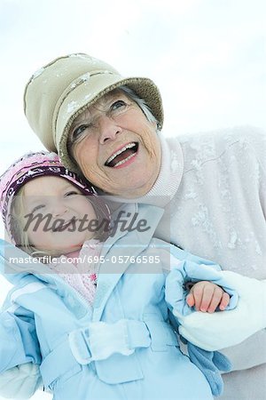 Senior Woman umarmen Enkelin im Schnee, beide Lächeln, Taille bis