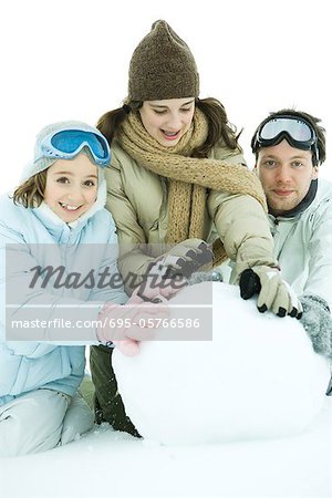 Trois jeunes amis accroupi dans la neige, il grande boule de neige, deux souriant à la caméra