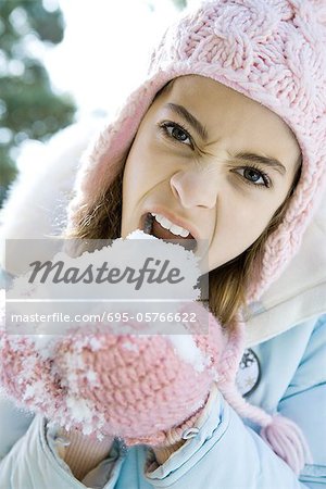 Preteen Mädchen essen Schnee aus mittened Händen, knurren und Blick in die Kamera