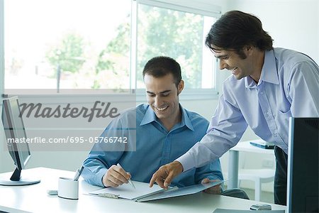 Two young businessmen looking at document together, laughing