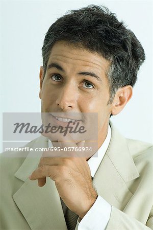 Businessman holding chin, looking up and smiling, portrait