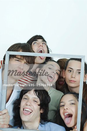 Group of young friends holding up picture frame, making faces at camera, portrait