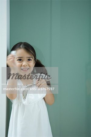 Little girl holding coin purse, one hand raised, smiling