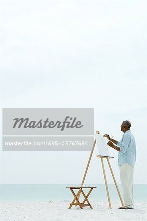 Homme senior, peinture sur toile à la plage, vue latérale