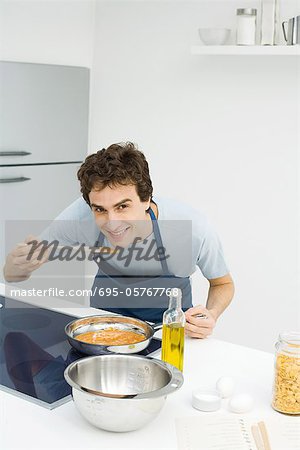 Mann in Küche, Kochen, Bücken auf Geschmack Sauce, lächelnd in die Kamera