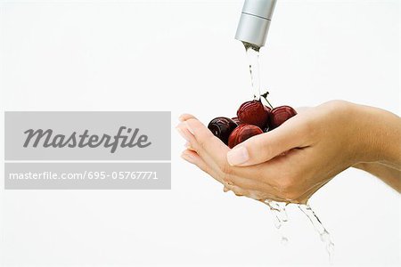Woman washing handful of tomatoes under faucet, cropped view of hands, close-up