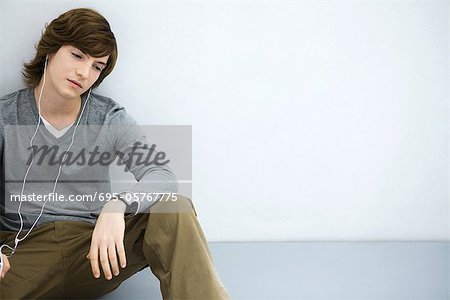 Young man sitting on the ground, listening to earphones, looking away