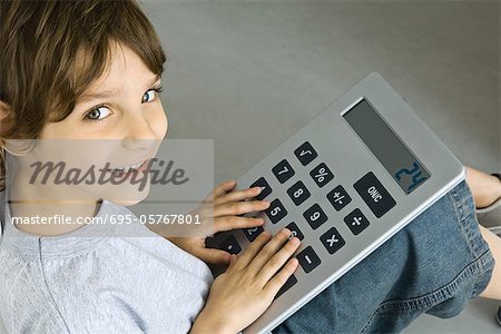 Little boy sitting on the ground, playing with large calculator, smiling at camera