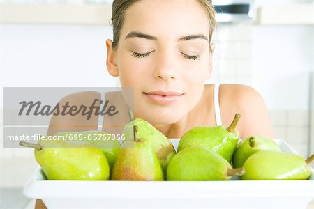 Young woman smelling fresh pears, eyes closed, close-up