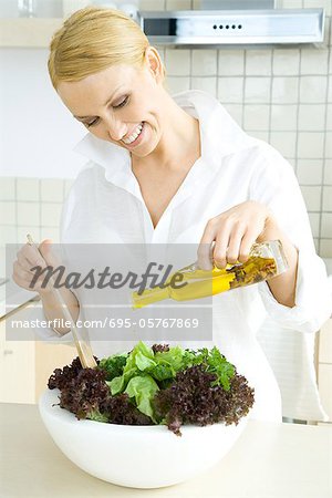 Frau in der Küche, gießt Olivenöl auf Salat