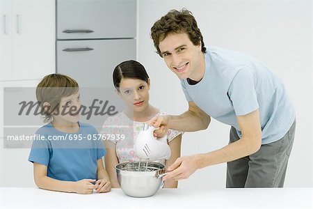 Man cooking with girl and boy, smiling at camera
