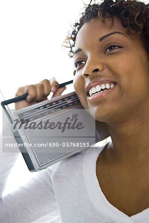 Young woman holding radio on shoulder, looking away, smiling