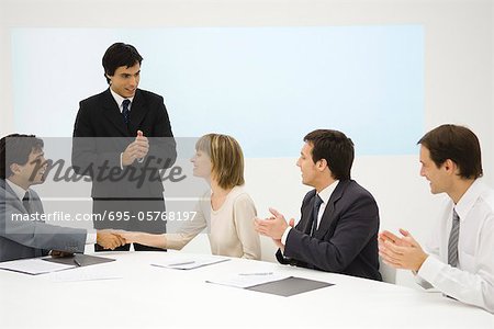 Business associates at conference table, two shaking hands, the others clapping