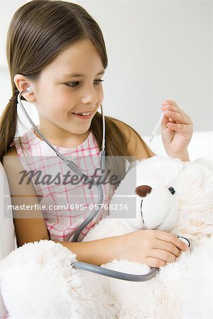 Little girl listening to teddy's bear's heart with stethoscope, looking at thermometer