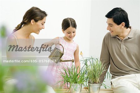 Little girl watering potted plants, parents watching, all smiling