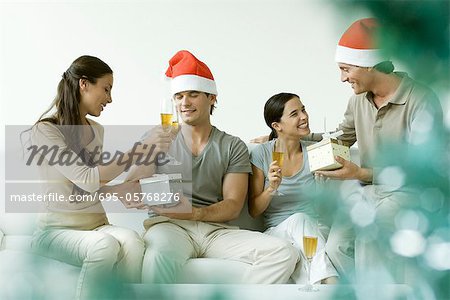 Deux couples d'échanger des cadeaux de Noël, buvant champagne, hommes portant des chapeaux Santa