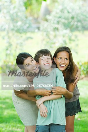 Mother embracing son and teen daughter, all smiling and looking up